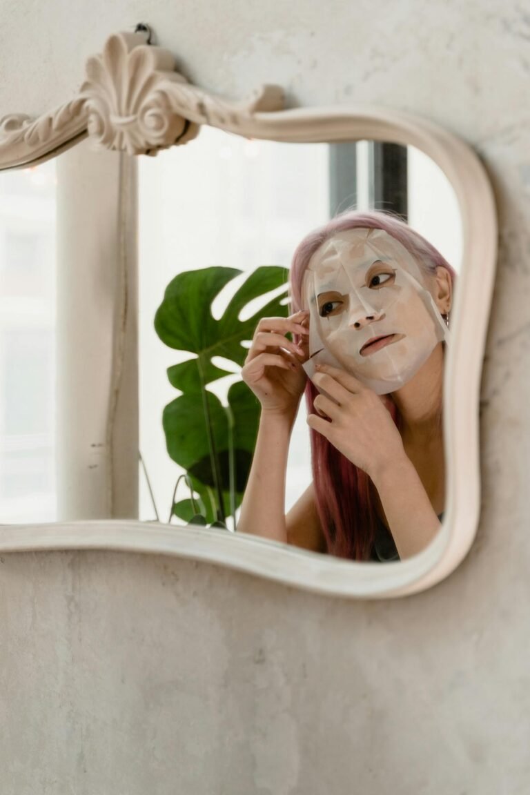 A woman looking at her reflection while applying a facial sheet mask at home.