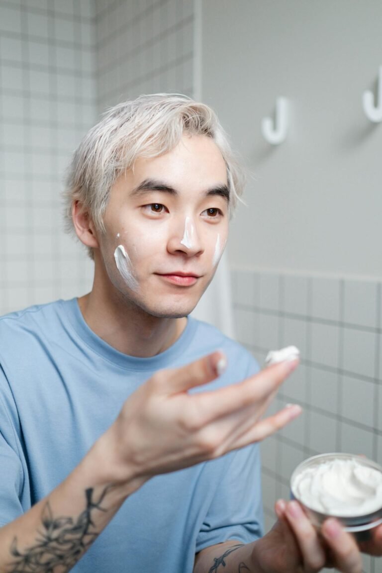 Portrait of a young man applying skincare cream in a contemporary bathroom.