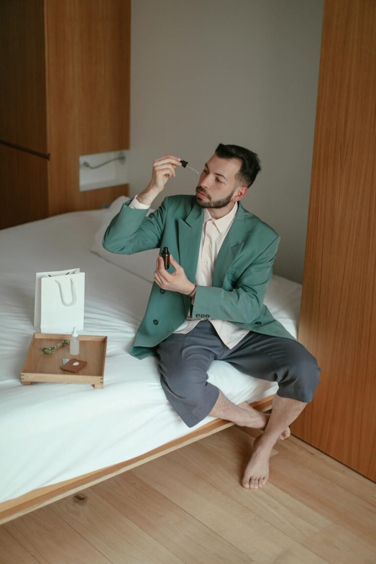 Young man applying skincare serum in a stylish home setting, emphasizing relaxation and self-care.